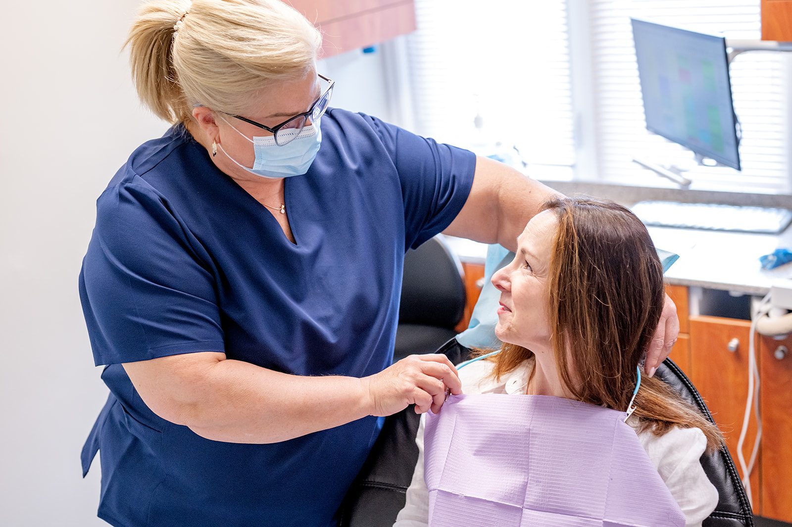 A dental assistant helping a patient settle comfortably into the chair